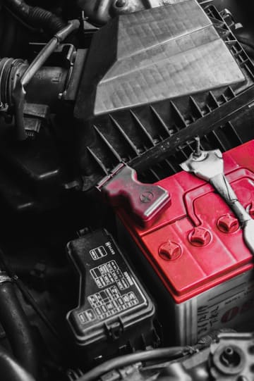 Close-up of a car battery and engine bay components under an open hood