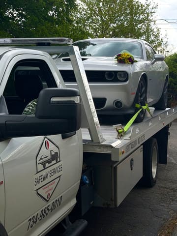 White Dodge Challenger strapped down with wheel straps on the deck of a Safeway Services flatbed