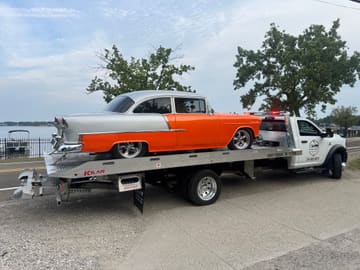 Rear view of a classic Chevrolet loaded on a tow truck beside a lake