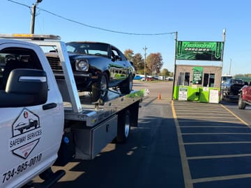 Black classic car strapped down on a Safeway Services flatbed at a drag strip entrance in Milan, Michigan