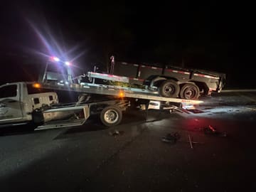 Tandem-axle dump trailer being winched onto a Safeway Services tow truck at night