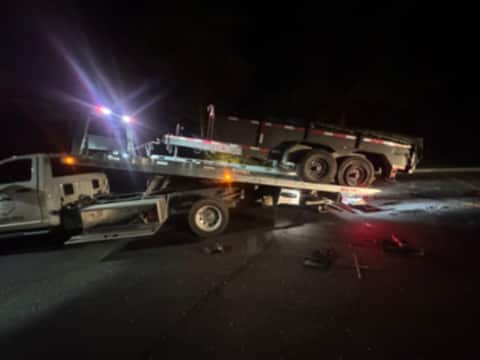Tandem-axle dump trailer being winched onto a Safeway Services tow truck at night