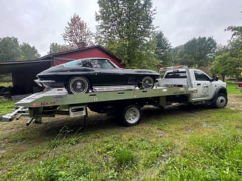 Black classic Corvette loaded on a Safeway Services tow truck in a field
