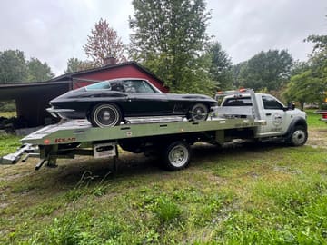 Black classic Corvette loaded on a Safeway Services tow truck in a field