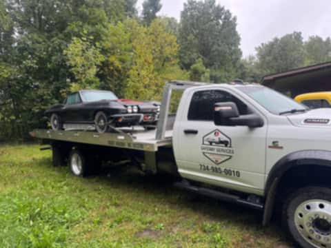 Front view of a Safeway Services flatbed truck with a black classic Corvette on the bed