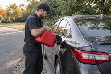 Technician pouring gasoline from a red fuel can into a car on a residential street