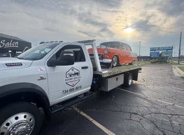 Safeway Services tow truck door with logo decal and phone number, loaded with an orange classic Chevrolet at sunset