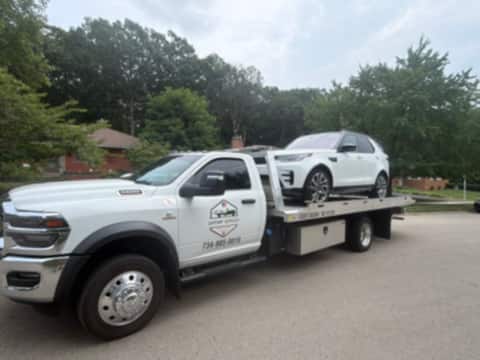 Safeway Services flatbed tow truck hauling a white Land Rover through a residential neighborhood
