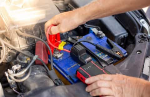Close-up of hands connecting red and black jumper cable clamps to a car battery terminal