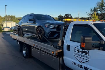Gray Mercedes-AMG SUV with bronze wheels strapped down at the wheels on a Safeway Services flatbed