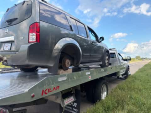 Nissan Pathfinder with a missing wheel loaded on a tow truck bed at the roadside