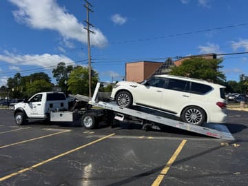 White Infiniti SUV being loaded onto a Safeway Services tow truck in a parking lot