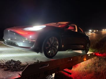Tesla loaded on a Safeway Services tow truck at night under work lights