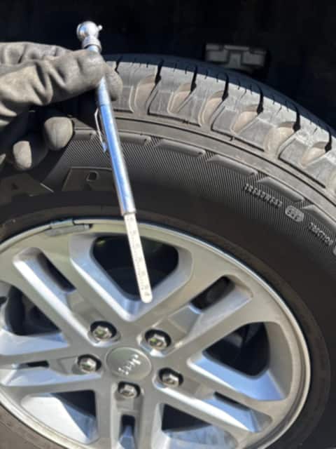 Gloved hand torquing a lug nut on a freshly mounted tire with a breaker bar