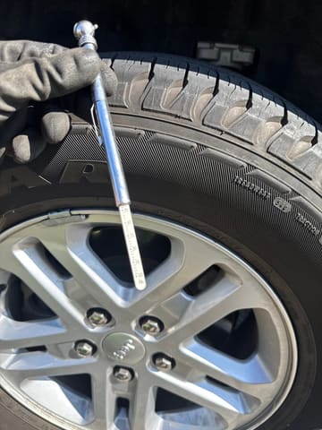 Gloved hand torquing a lug nut on a freshly mounted tire with a breaker bar