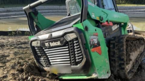 Bobcat compact track loader tipped forward and sunk in deep mud on a job site