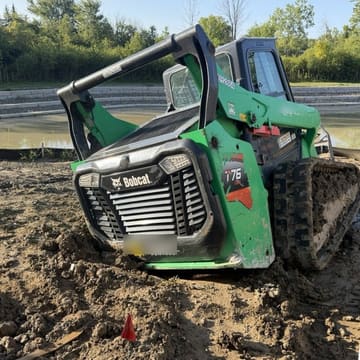 Bobcat compact track loader sunk in deep mud on a job site, tipped forward with one track buried